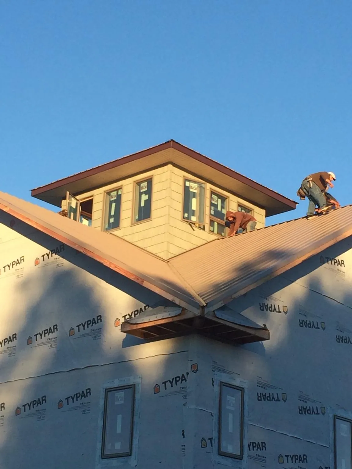 Roofers working around a rooftop cupola on a new metal roof at sunset — Roof Waterproofing in Harrison by Roofing Brothers